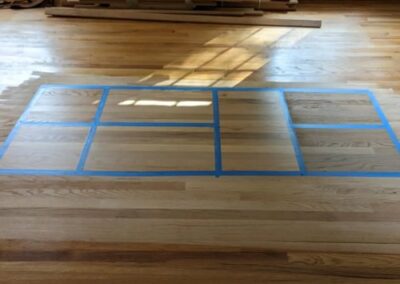 Image of a floor about to be refinished with painters tape in a grid for showing different stains