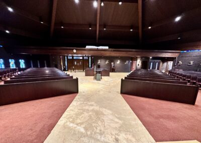 Concrete subfloor exposed after carpet removal in St Thomas More Church sanctuary showing phased installation area