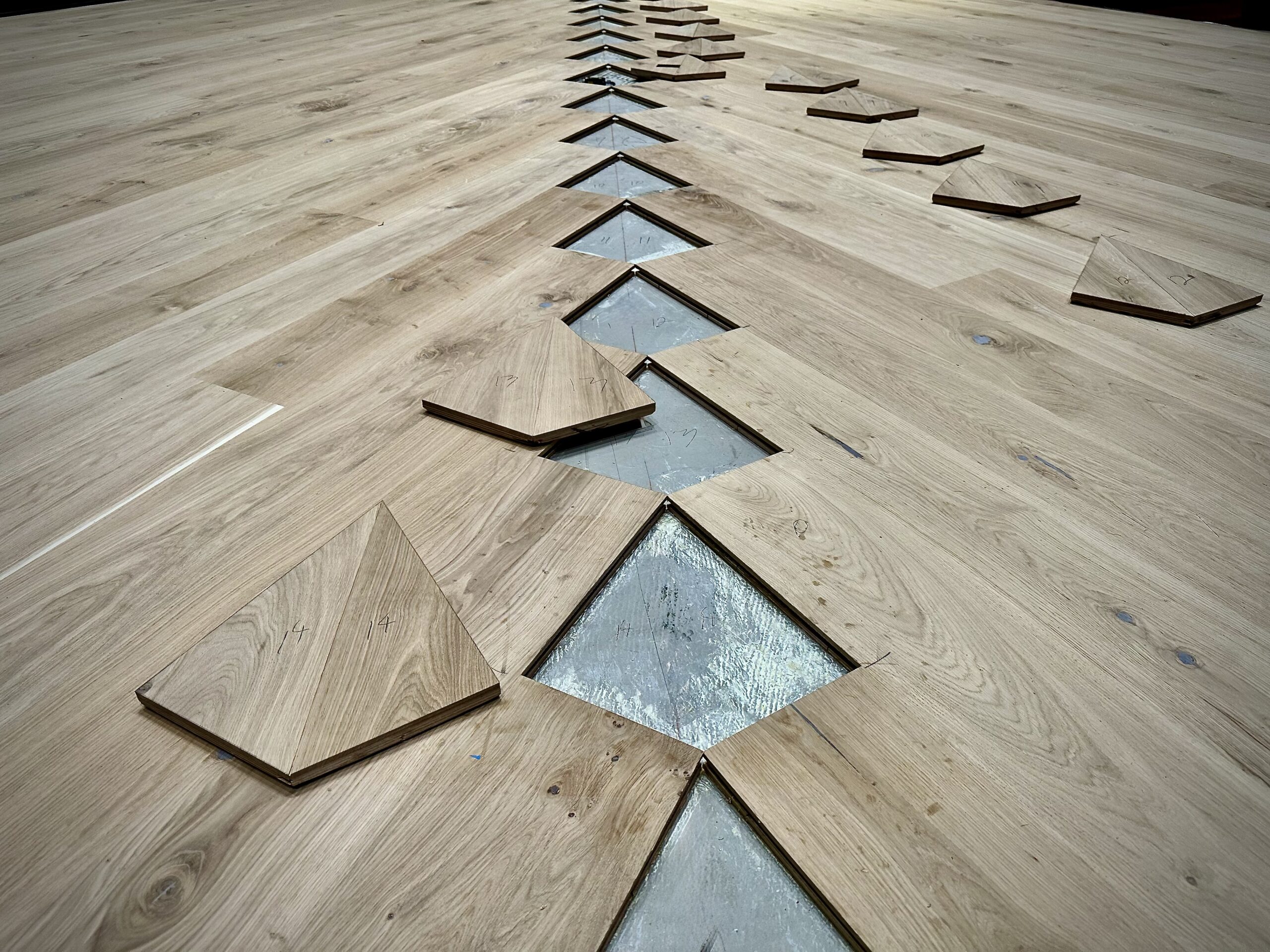 Rows of hand-cut walnut and European white oak diamond inlays staged beside their corresponding floor locations