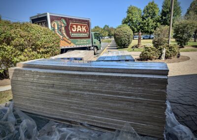 Plastic-wrapped bundles of European white oak flooring staged outside Saint Thomas More Church with JAK Wood Flooring box truck in the background